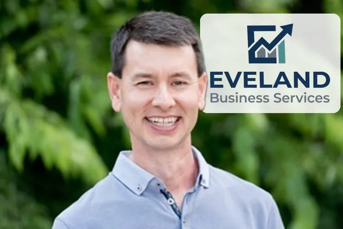 Eric Eveland, smiling outdoors, with the Eveland Business Services logo behind him